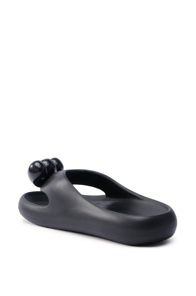The AKIRA COMPASSION BLACK SANDAL features a sleek design with an EVA upper and unique thong toe, complemented by a rounded toe knob and open heel. Its smooth, rubber-like surface enhances its minimalist aesthetic, ideal for contemporary styling.