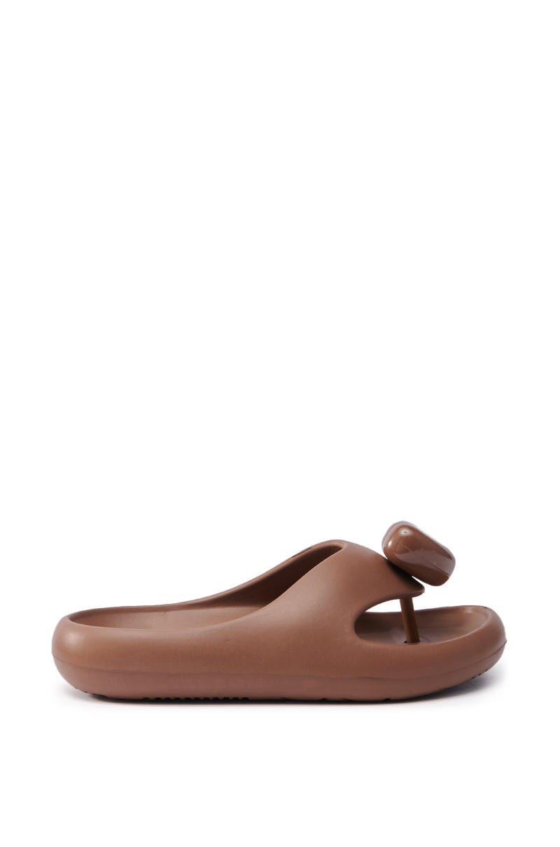 The AKIRA COMPASSION BROWN SANDAL showcases a slide-on style with a rounded, elevated sole and minimalist elegance, featuring a single thick strap and almond thong toe against a plain white background.