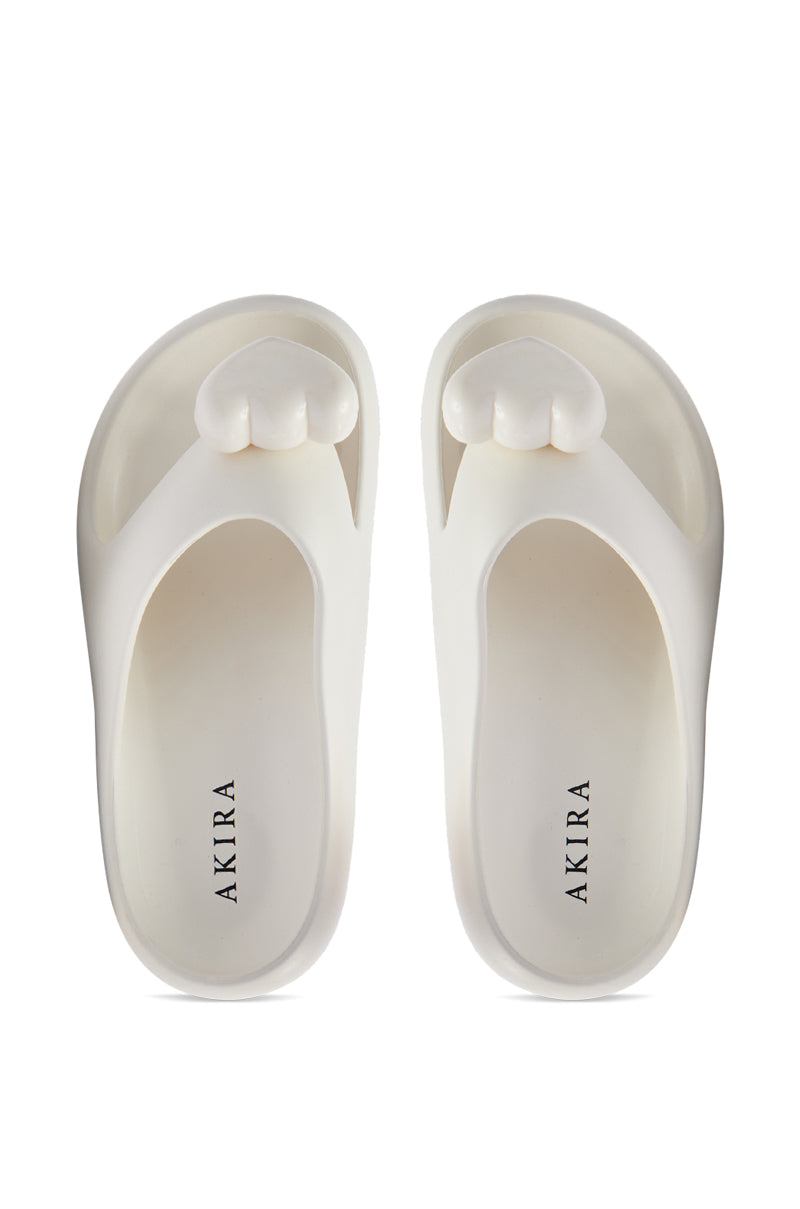 The AKIRA COMPASSION WHITE SANDAL features white slides with thick soles, cushy material, a rounded toe design, and "AKIRA" on the footbed, combining comfort and style for everyday wear.
