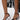Someone wearing the AZALEA WANG CORABELLA BLACK NOVELTY HEEL SANDAL with a faux leather upper, circular sculpted heels, and ankle straps, paired with a sheer black floral lace skirt.