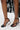 Someone wearing the AZALEA WANG CORABELLA BLACK NOVELTY HEEL SANDAL with a faux leather upper, circular sculpted heels, and ankle straps, paired with a sheer black floral lace skirt.