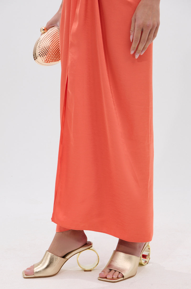 A person wearing a coral maxi dress and AZALEA WANG CORABELLE GOLD NOVELTY HEEL SANDALS with an open square toe stands against a white background, holding a small gold clutch. 1