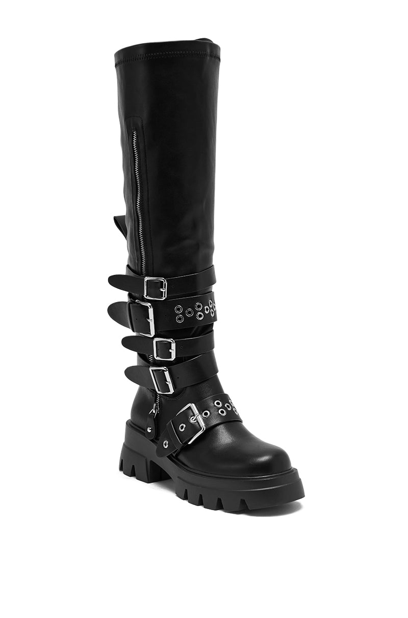 The AZALEA WANG CORDOVAN BLACK BELTED BOOT is a black knee-high boot with a chunky sole, multiple silver buckles, grommets, decorative straps, and a side zipper.
