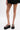 A woman stands against a plain white background wearing a short black ruffled skirt and the AZALEA WANG CORLISS LEOPARD FLATFORM SANDAL featuring a cushioned faux leather insole.