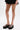 A person in a black pleated skirt and AZALEA WANG CORLISS LEOPARD FLATFORM SANDALS with cushioned faux leather insoles stands against a plain white background.