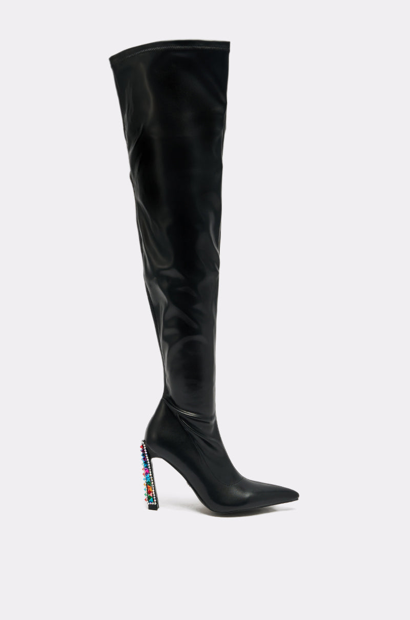 The AZALEA WANG COSMIC BLING BLACK BOOT features black faux leather, a pointed toe, and an over-the-knee silhouette. Its tall block heel is embellished with colorful rhinestones and is displayed on a plain light background.
