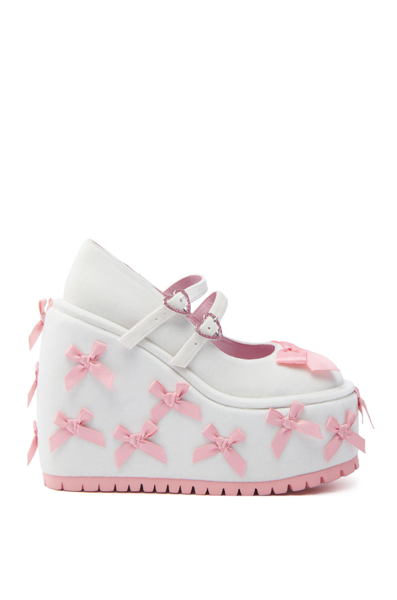 The KOI FOOTWEAR A COURTSHIP OF BOWS PINK WEDGE SNEAKER features a velvet-textile white upper, pink trim, Mary Jane foot straps with heart buckles, chunky pink platform wedge, and pink bows on the sole and upper for a cute finish.