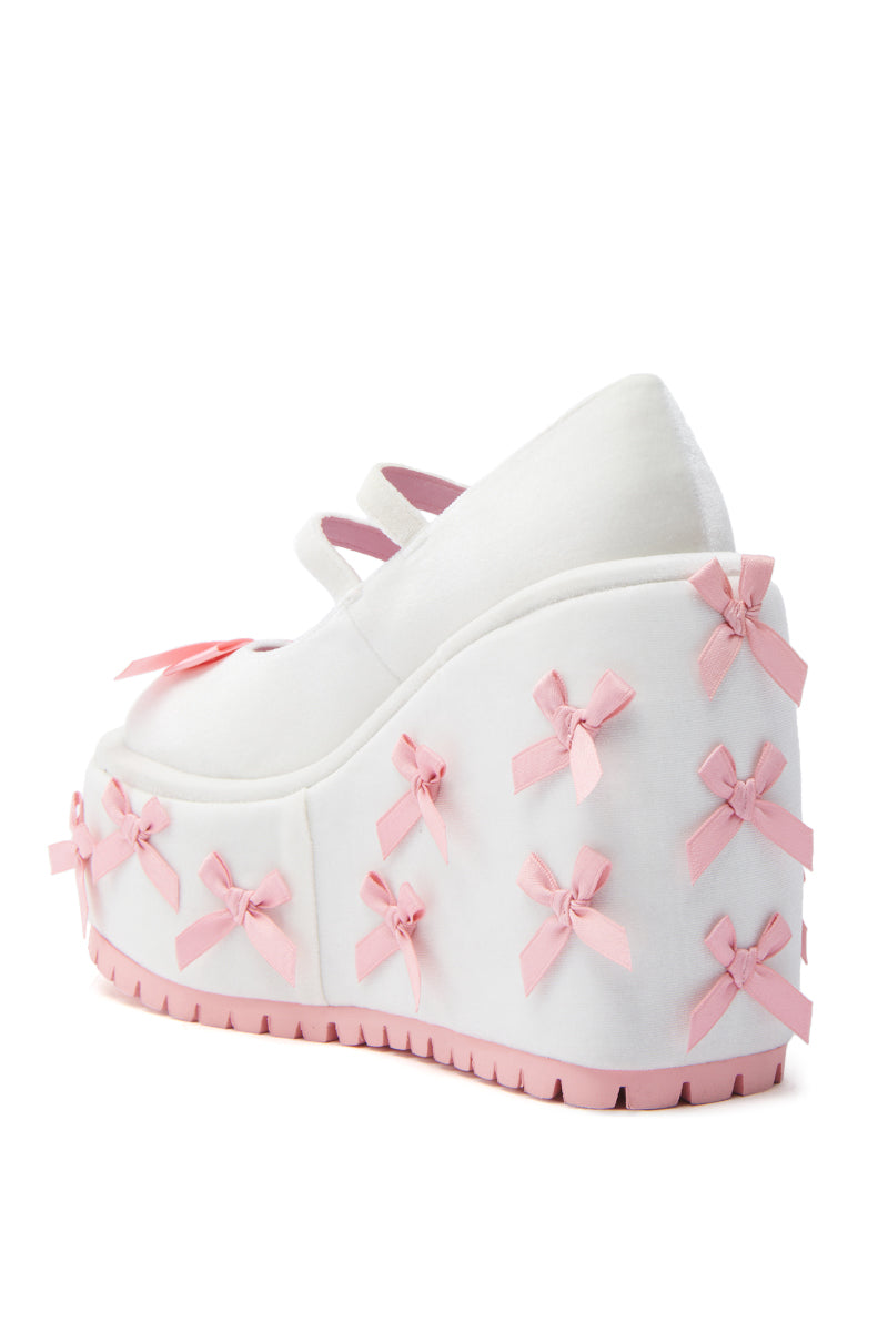 The KOI FOOTWEAR A COURTSHIP OF BOWS PINK WEDGE SNEAKER features a velvet upper, thick pink platform wedge sole, Mary Jane straps, a large front bow, and small pink bows for a sweet yet modern look.