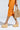 Person in an orange ruched dress, holding a woven handbag, wearing AZALEA WANG COVA beige wedge heel espadrilles with a platform sole, walking against a plain background.