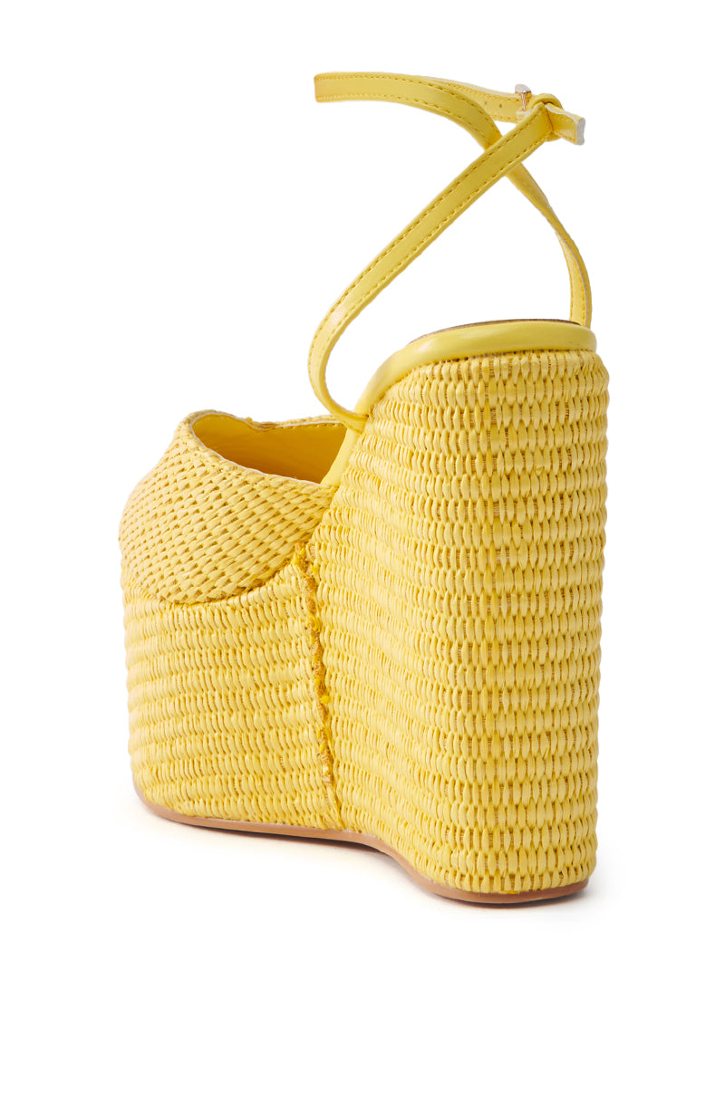 The AZALEA WANG COVA YELLOW WEDGE features a close-up view of its yellow platform wedge sandal with an ankle strap, highlighting its wicker-inspired woven texture for a summery feel. The tall heel complements the vibrant color and intricate design.