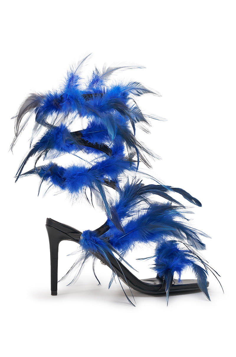 The AKIRA GOLD COVERT FEATHER EMBELLISHED SPIRAL STRAP STILETTO SANDAL features a bold black heel with vibrant blue and black feathers that spiral around the ankle, creating a striking high-fashion statement. 4