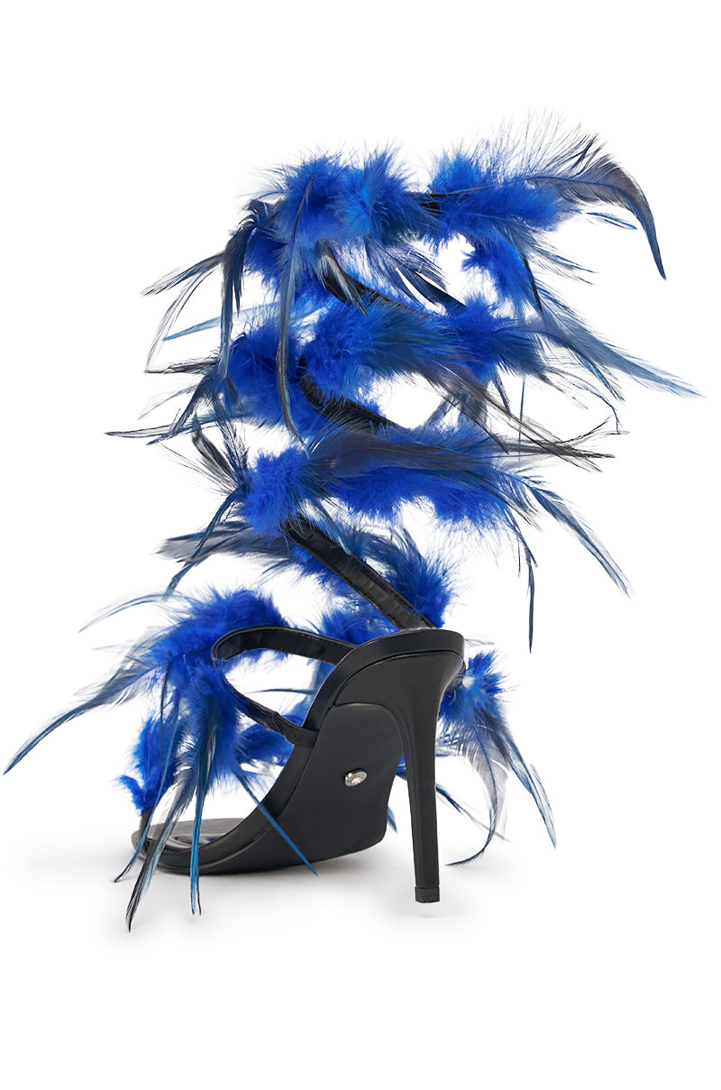 The AKIRA GOLD COVERT FEATHER EMBELLISHED SPIRAL STRAP STILETTO SANDAL features striking black and blue feathers winding from ankle to calf, making this high-heeled design a bold, glamorous statement piece. 6