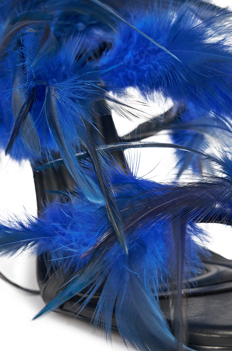 Close-up of the AKIRA GOLD COVERT FEATHER EMBELLISHED SPIRAL STRAP STILETTO SANDAL, featuring vibrant blue feather accents on the spiral straps for a bold, textured high-fashion look against a white background. 7