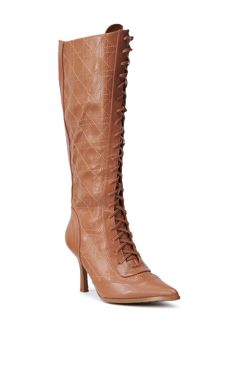 Introducing the CREATOR TAN LACE UP STILETTO BOOT: a stylish knee-high boot featuring a tall shaft with a brown finish, pointed toe, and elegant crisscross lacing up the front. The luxurious faux leather design is highlighted by a quilted pattern for added sophistication.