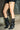 A person stands on concrete near a brick wall and metal fence, wearing black pinstriped shorts and AZALEA WANG CRESSINDA BLACK GUNMETAL DOME STUD STILETTO BOOTIE.