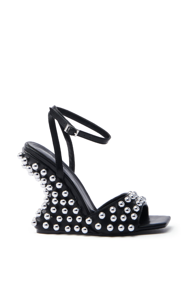 The AZALEA WANG CYBELE BLACK EMBELLISHED WEDGE SANDAL is a bold statement piece crafted from faux leather, featuring an ankle strap with buckle closure, peep toe design, and silver stud embellishments on the platform and heel.