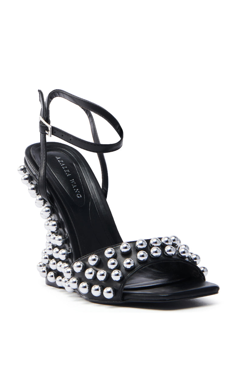 The AZALEA WANG CYBELE BLACK EMBELLISHED WEDGE SANDAL is a stylish faux leather high-heeled sandal adorned with silver studs on the straps and heel, featuring an embellished heel and a secure buckle ankle strap.