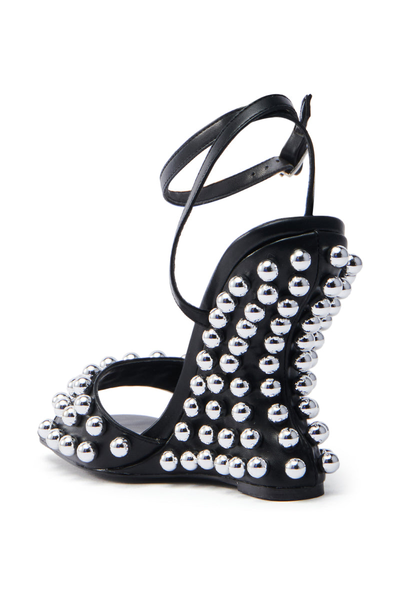 The AZALEA WANG CYBELE BLACK EMBELLISHED WEDGE SANDAL features sleek faux leather with an arched, embellished heel. Shiny silver studs adorn the heel and straps for added glamour, while an ankle strap ensures a secure fit.
