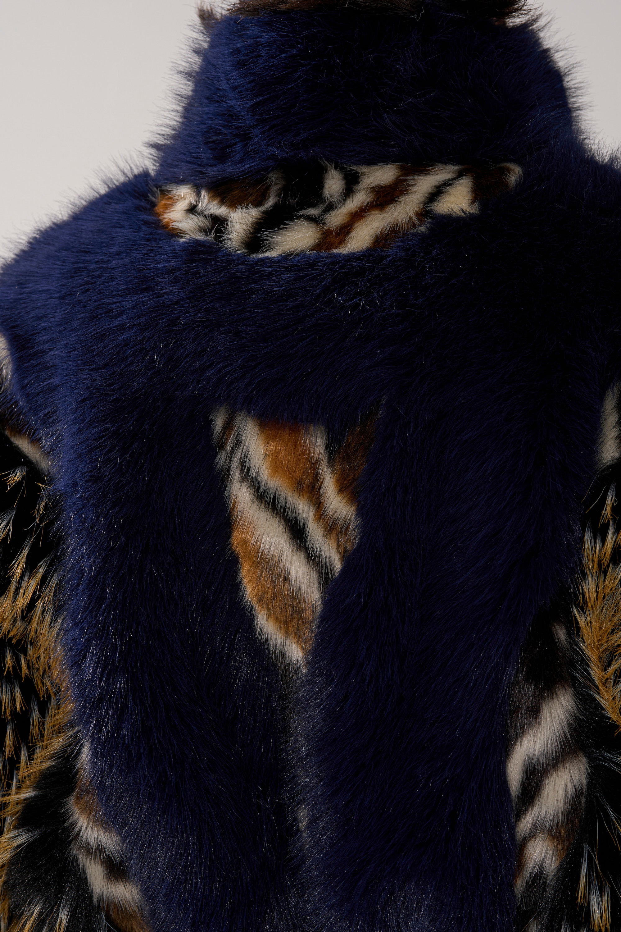 A close-up of the CYCLONE PATCHWORK FAUX FUR, a dark blue faux fur scarf paired with an orange, black, and white tiger print cropped jacket, showcasing a chic silhouette.