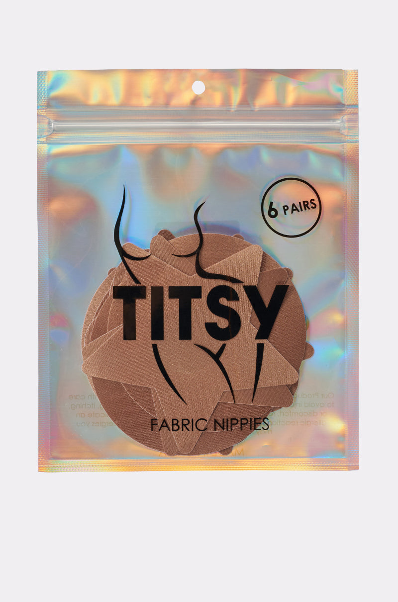 A holographic resealable pouch holds six pairs of TITSY TAN NIPPY 6 PACK fabric nipple covers with adhesive backing. Minimalist packaging displays a line drawing of a torso and the words "TITSY" and "FABRIC NIPPIES. 3