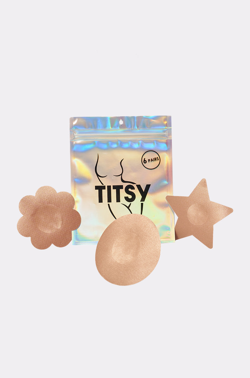 The TITSY TAN NIPPY 6 PACK includes six nude adhesive nipple covers in flower, star, and circle shapes, shown in front of a holographic resealable pouch labeled "TITSY" with a minimalist torso line drawing. 0