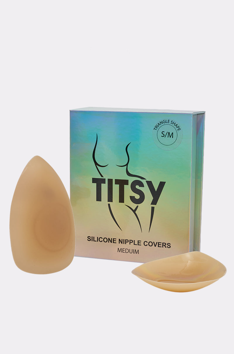 A box labeled "TITSY TRIANGLE SILICONE NIPPIE COVER" is positioned behind two tan, triangle-shaped silicone nipple covers on a plain white background.