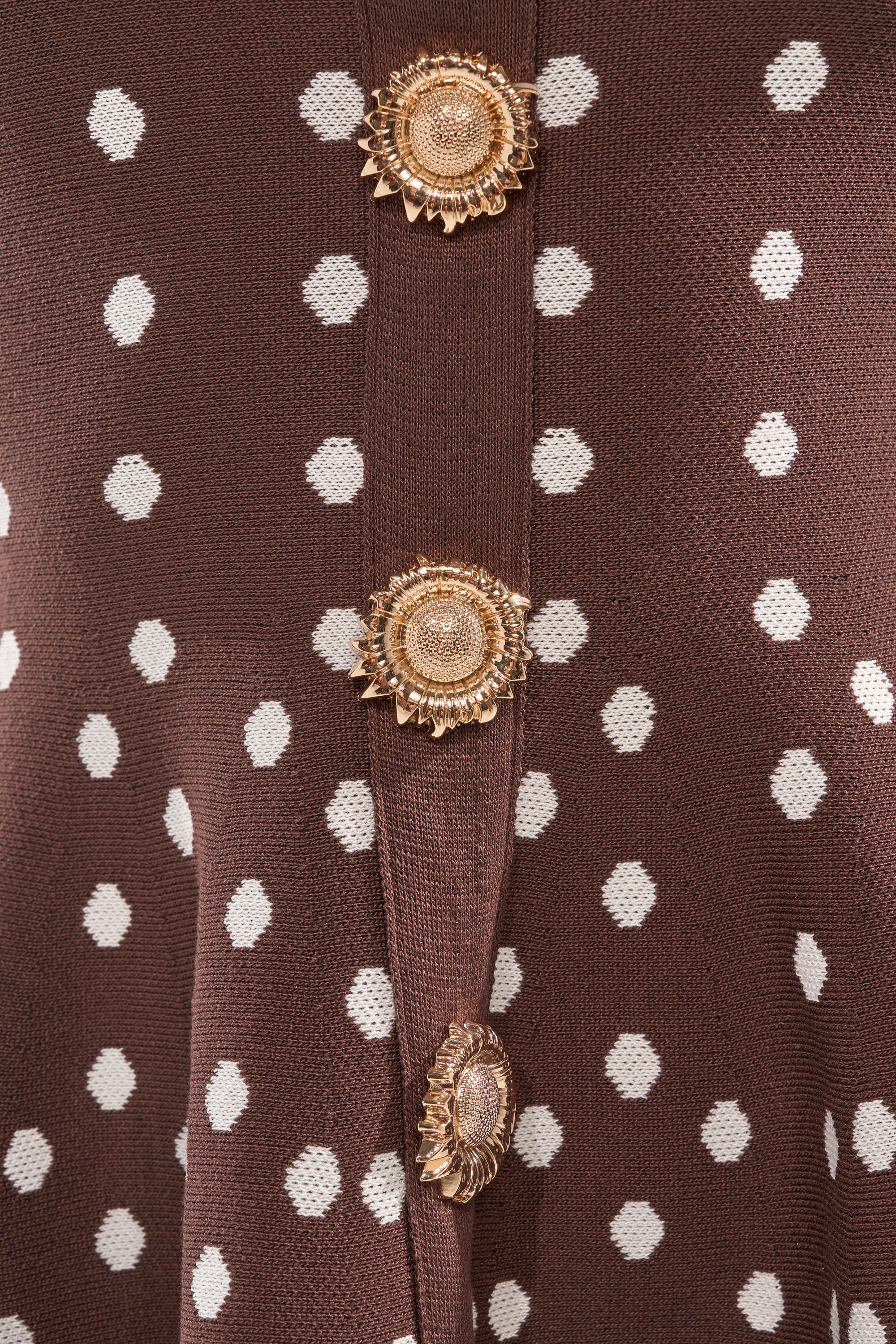 Close-up of the BABY GIRL POLKA DOT HALTER MINI DRESS, a brown mini dress with white polka dots and three ornate gold flower-shaped buttons arranged vertically along a seam. 7