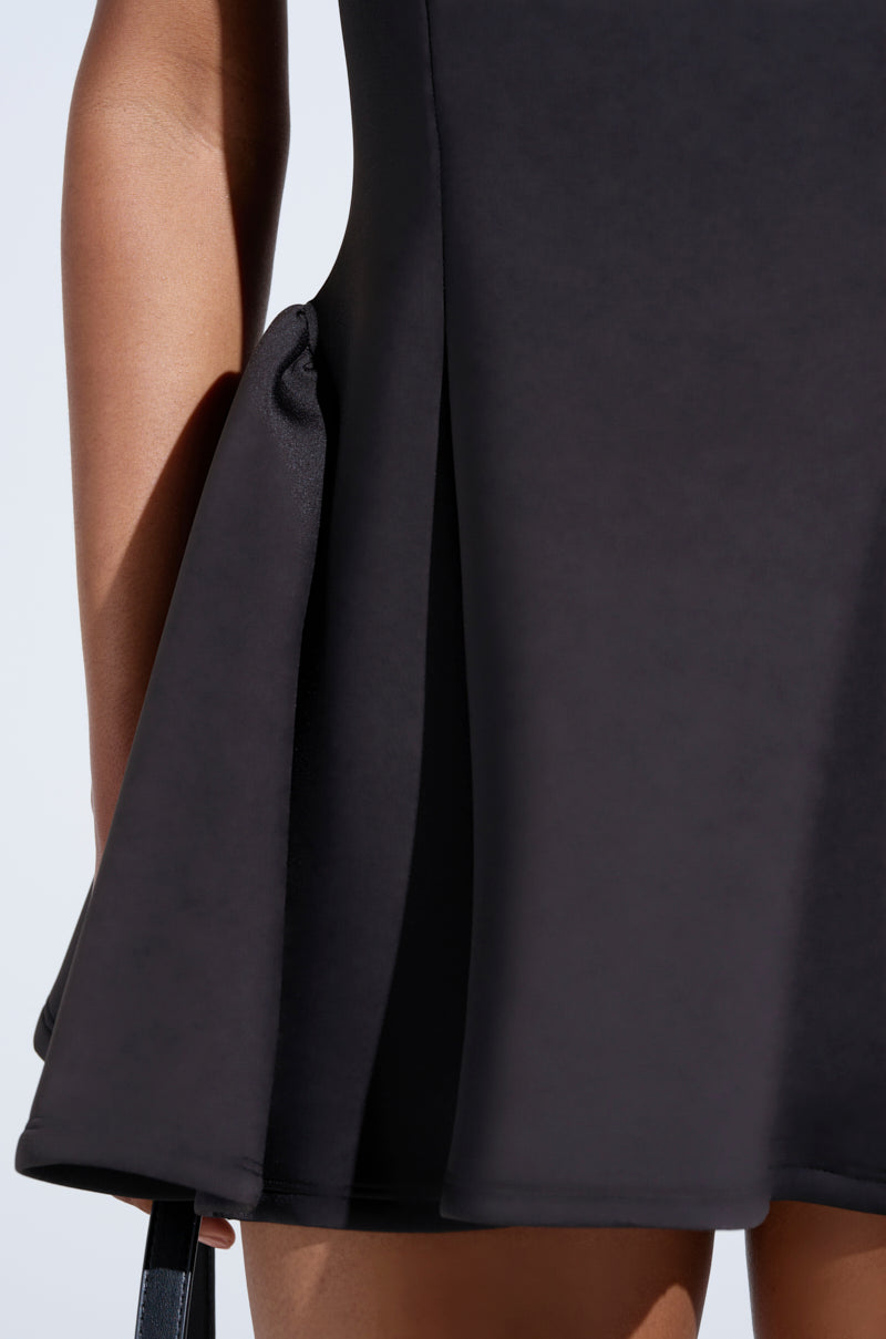 A close-up shows a person in the CELINE BANDAGE MINI DRESS, a chic black sleeveless skater silhouette with a pleated, flared skirt. Cropped at the hip against a plain light background, it highlights this stylish LBD's elegance. 5