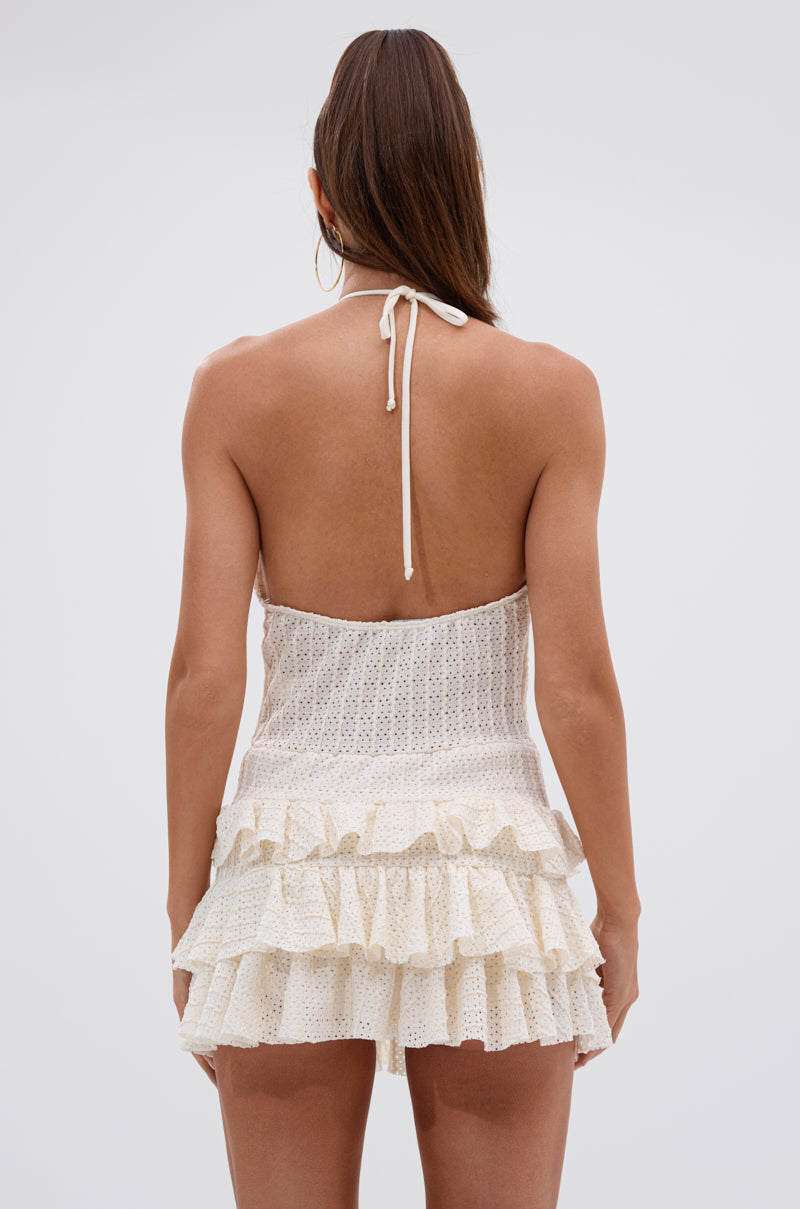 A woman with long brown hair, wearing the SUMMATIME FINE RUFFLE MINI DRESS—halter-neck, backless with layered ruffle skirt—stands facing away against a plain light gray background. 3