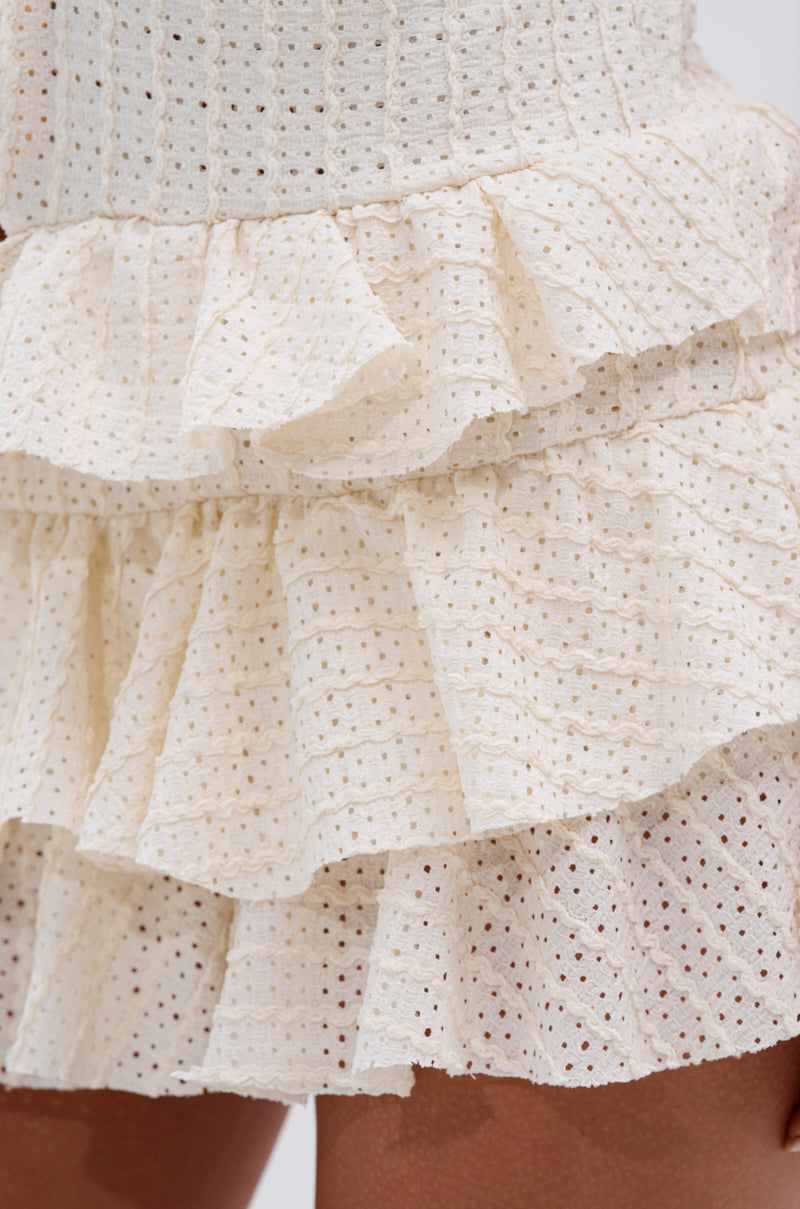 Close-up of the SUMMATIME FINE RUFFLE MINI DRESS in cream, featuring eyelet lace, layered ruffles, and textured fabric with small holes for an airy look. The mini skirt highlights tan skin. 6