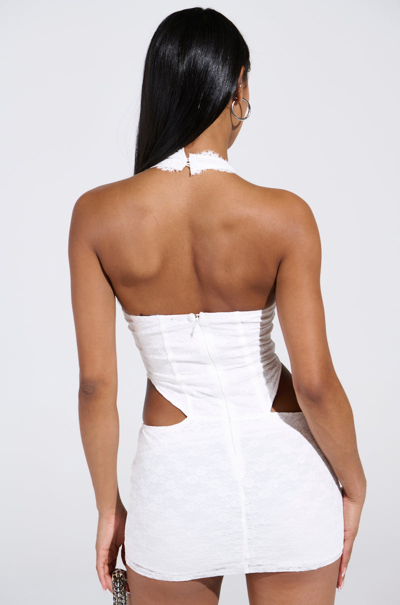A woman with long straight hair wears the SOPHIE MINI DRESS, a white, backless mini dress with side cutouts and a plunging halter neckline, standing with her back to the camera against a plain light background.