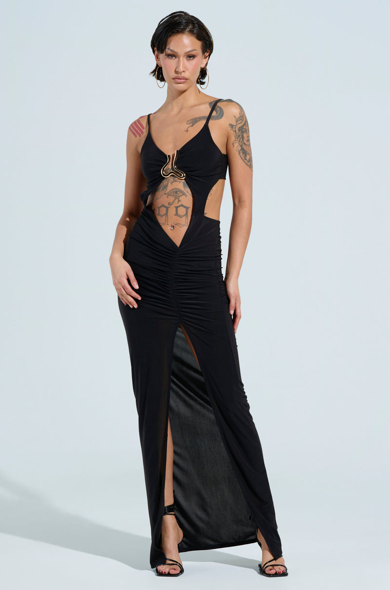 A person exudes confidence in the LAY IT LOW SLINKY MAXI DRESS, featuring cut-out details and a thigh-high slit that's ideal for evening wear. The unique waist design complements their visible tattoos and short styled hair, adding an edgy twist to their chic ensemble.