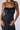 A person is wearing the Work It Girl Knit Utility Dress, a fitted, sleeveless black denim piece featuring front pockets and a zipper closure. Adorned with tattoos on their arms and accessorized with a chunky metallic necklace, they have their hands casually positioned in front of them, perfectly capturing the dress's effortless style.