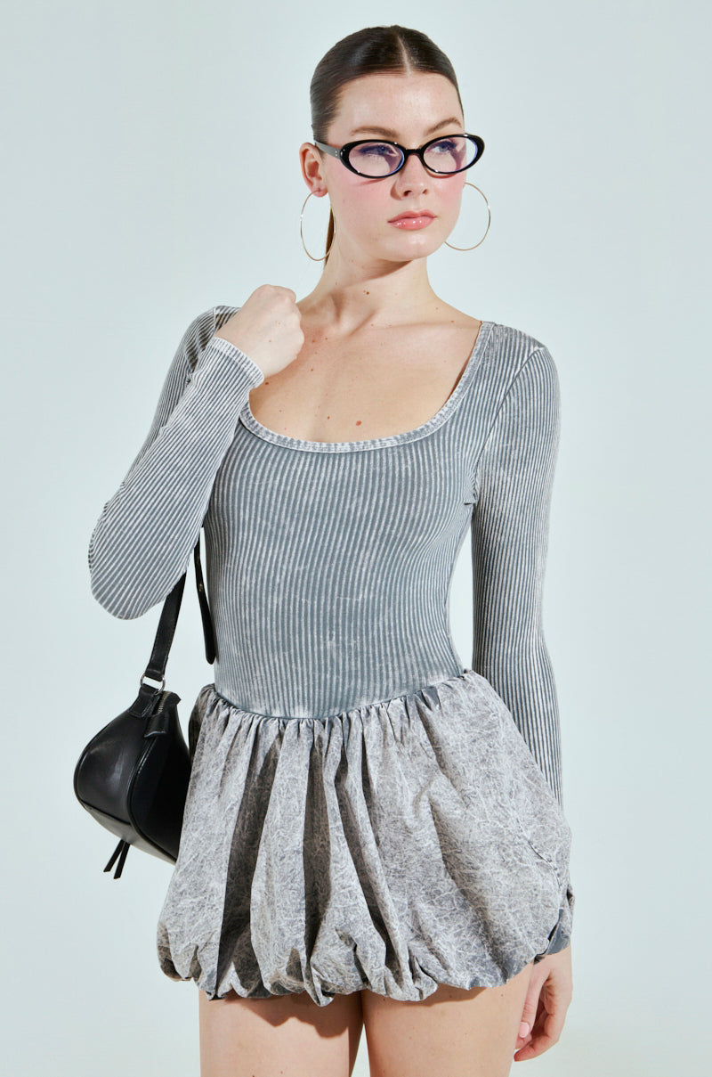 Someone in a "Give Me A Little Mini Dress" in light gray poses against a light background, accessorized with black cat-eye glasses, hoop earrings, and a small black shoulder bag.
