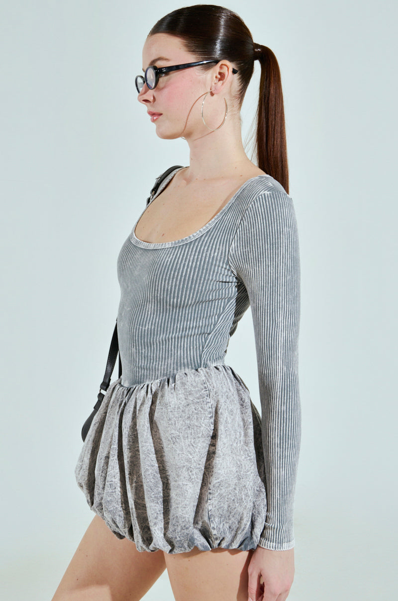 A confident person with a ponytail and glasses stands sideways against a white background, wearing the "GIVE ME A LITTLE MINI DRESS IN LIGHT GREY" and large hoop earrings.