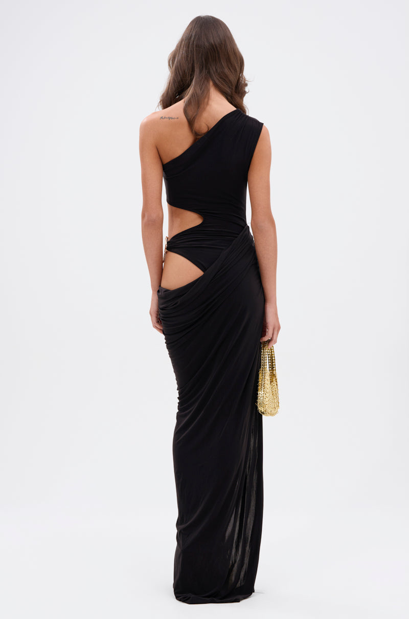 A woman with long brown hair models the ONLY ME CUT-OUT MIDI DRESS IN BLACK, a one-shoulder, asymmetrical cut-out evening gown in stretchy fabric. She holds a gold clutch and stands with her back to the camera against a white background.