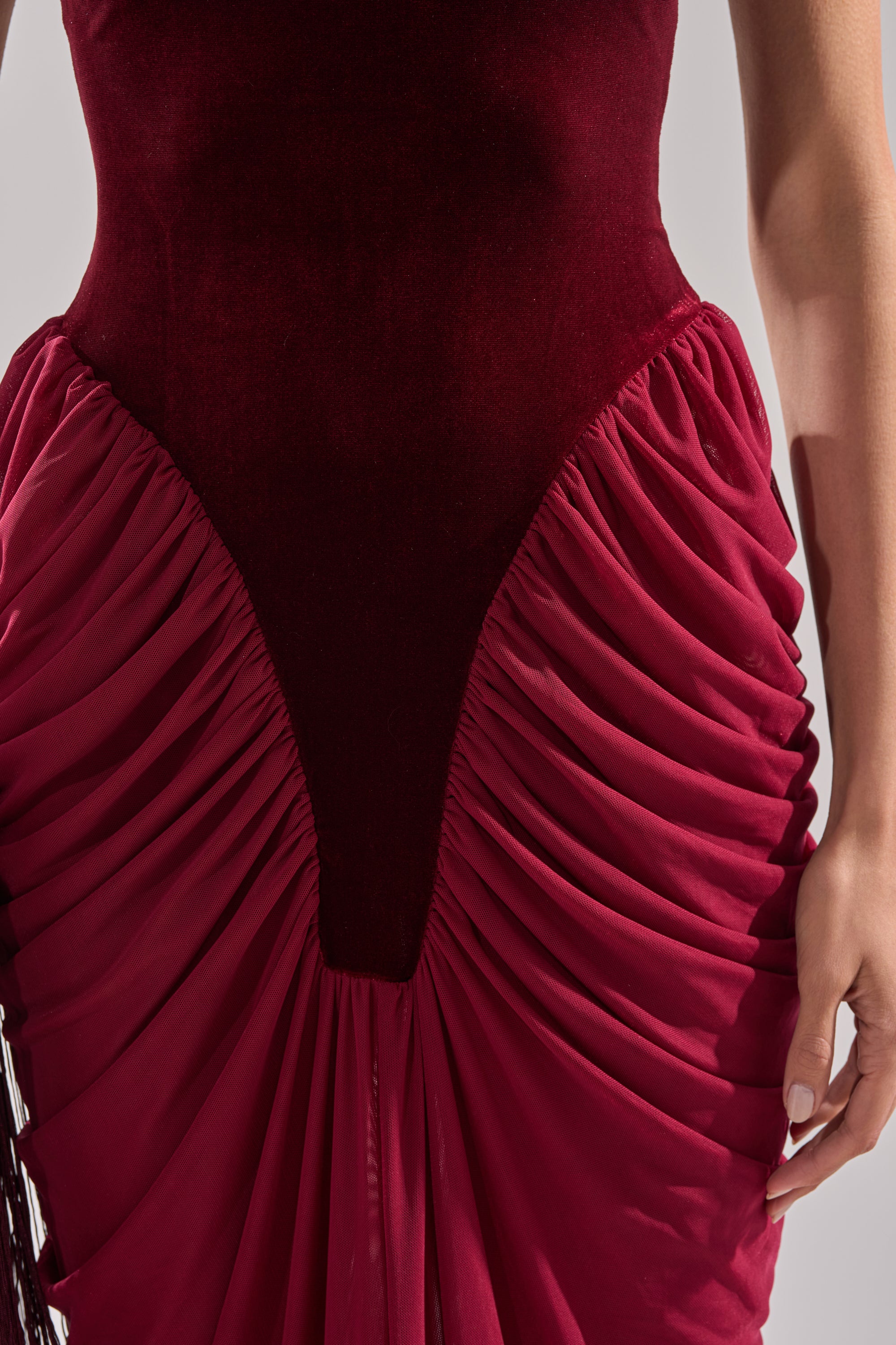 Wearing the BABY ITS COLD OUTSIDE VELVET RUCHED MAXI DRESS in deep red, with a ruched skirt, perfect for formal events; shown from shoulders to mid-thigh with one arm visible at their side.