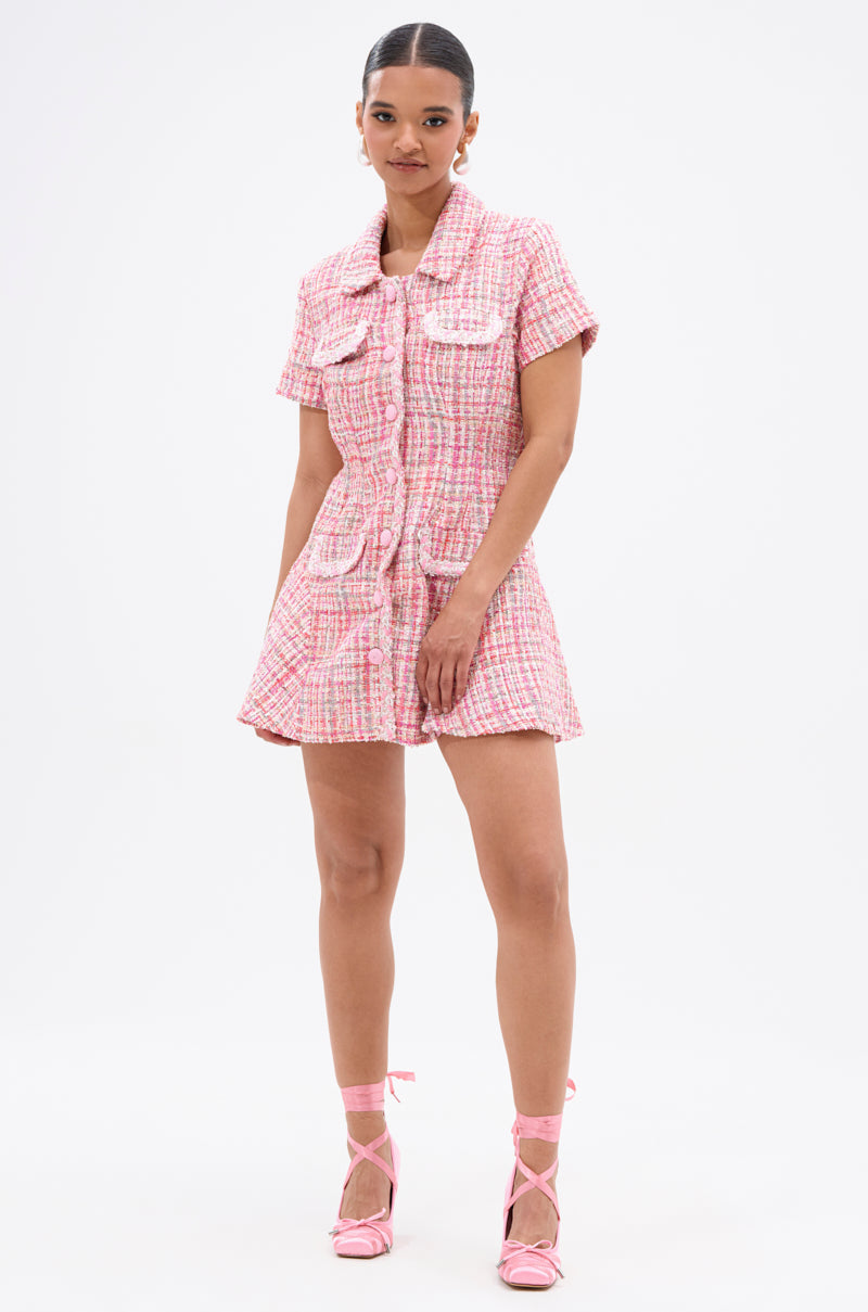 A woman poses against a white background in the TAKE NOTES TWEED MINI DRESS IN PINK, featuring structured short sleeves, large front pockets, and a collar. Her hair is tied back and she wears matching pink strappy heels.