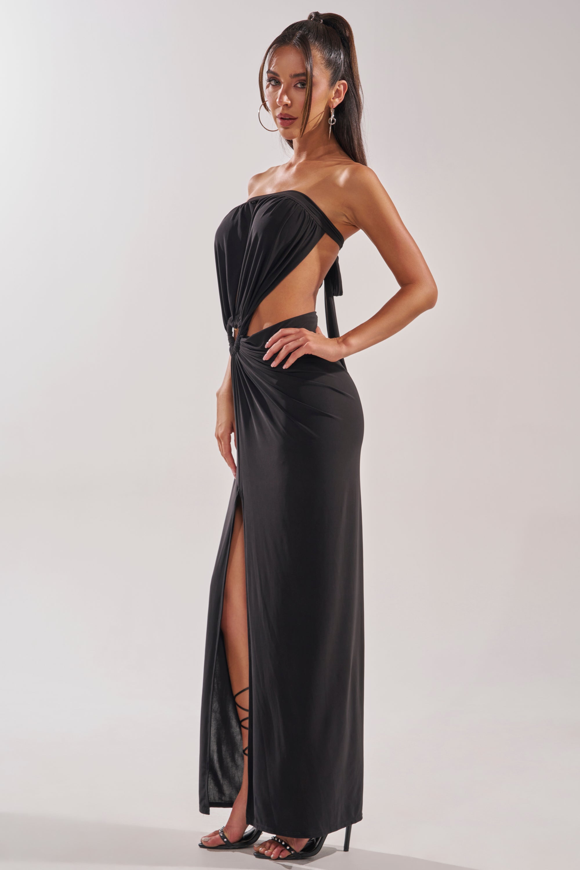 A woman models the DONT BREAK MY HEART STRAPLESS MAXI DRESS, featuring a side cutout and high leg slit. She completes the look with strappy black heels, hoop earrings, and a high ponytail. 4