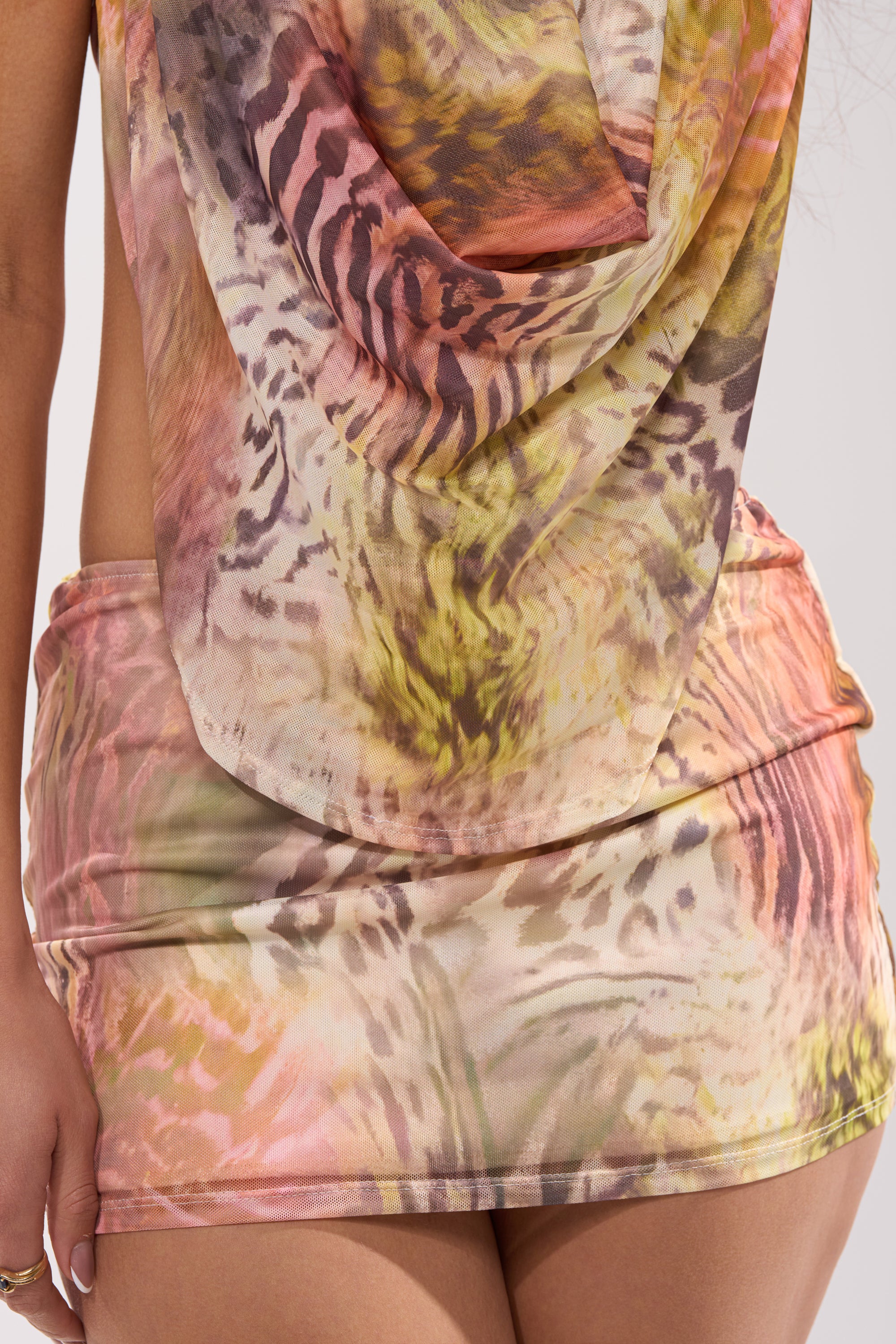 A close-up of a person wearing the I BITE BACK MINI DRESS, featuring a vibrant animal-inspired print in pink, yellow, brown, and white tones with a draped cowl neckline for a bold statement look. 9