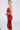 A woman poses in side profile wearing the ROSEY MIDI DRESS, a curve-hugging, sleeveless red and black floral dress with thin straps. Her hair is styled in a sleek bun, accessorized with large hoop earrings against a plain light background.