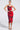 A woman models the ROSEY MIDI DRESS, a fitted, sleeveless red and black floral dress with thin straps and a curve-hugging silhouette. She pairs it with hoop earrings and strappy black heels against a plain white background.