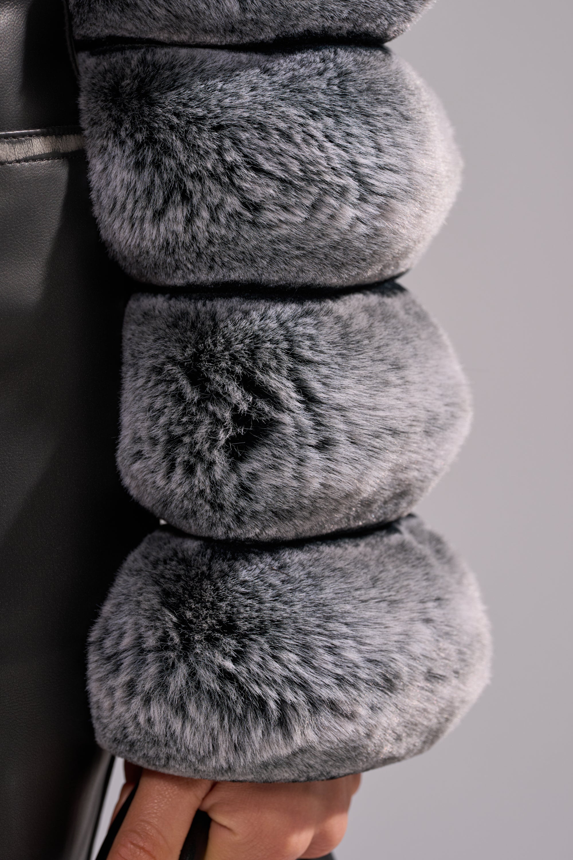 Close-up of three round sections of POPCORN FAUX FUR IN GREY, showing its soft texture and subtle light-dark patterns, stacked vertically against a smooth, dark background. 10