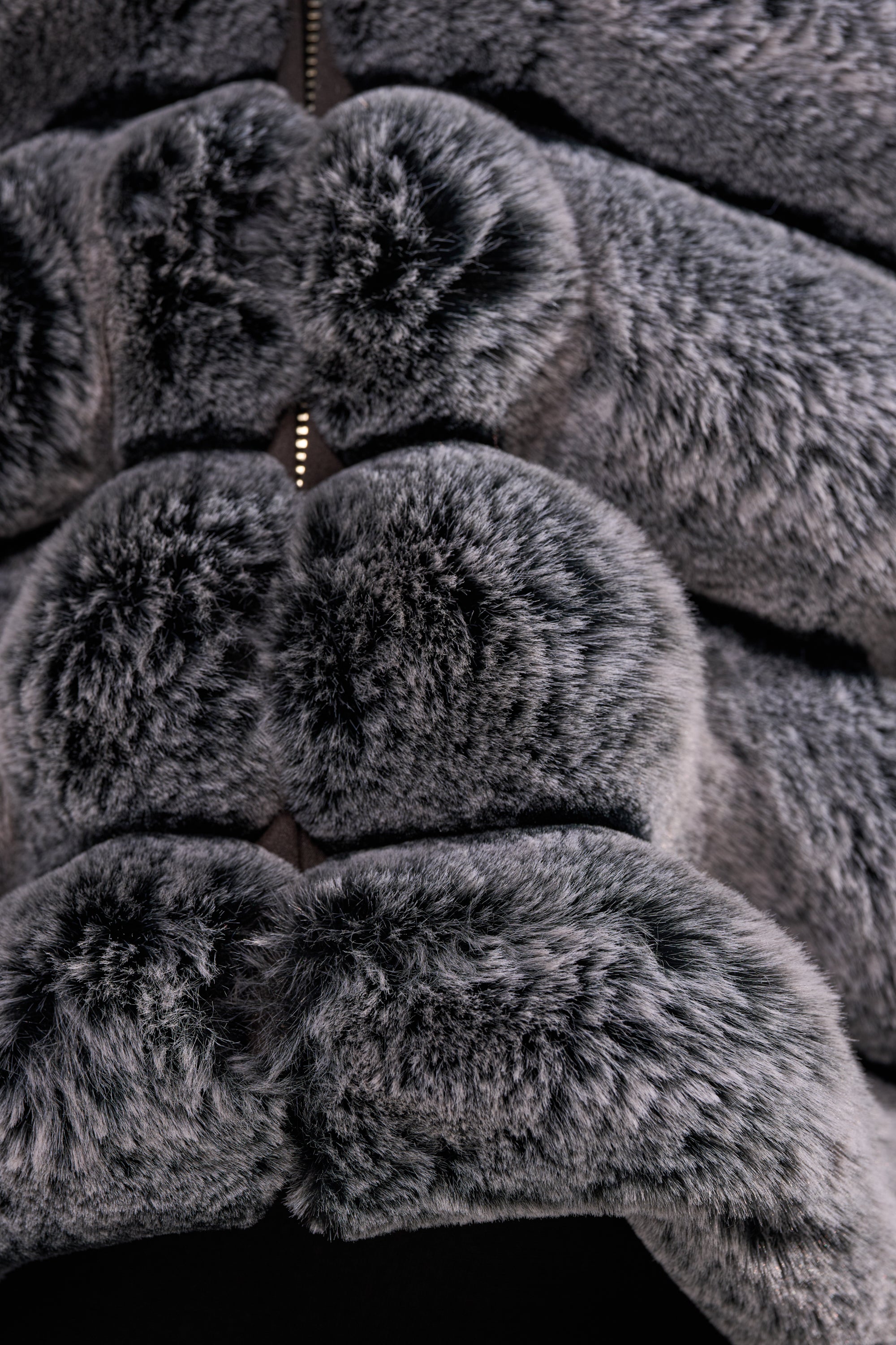 Close-up of the POPCORN FAUX FUR IN GREY jacket featuring soft, plush, horizontally padded sections and a visible metal zipper down the center. 11