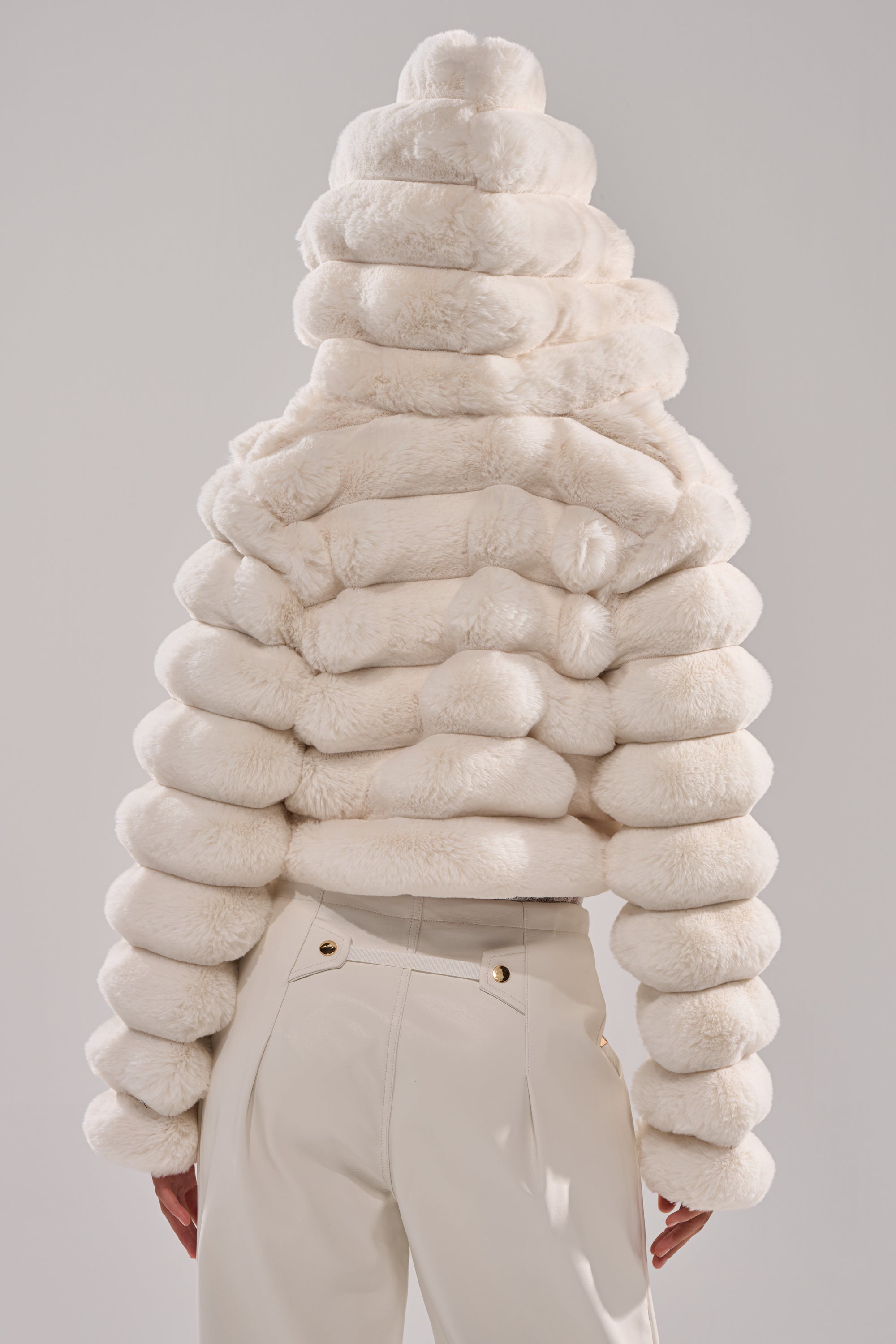 A person seen from behind wears the POPCORN FAUX FUR IN WHITE jacket, featuring plush, segmented faux fur resembling stacked rings, paired with high-waisted white pants against a plain light background. 7