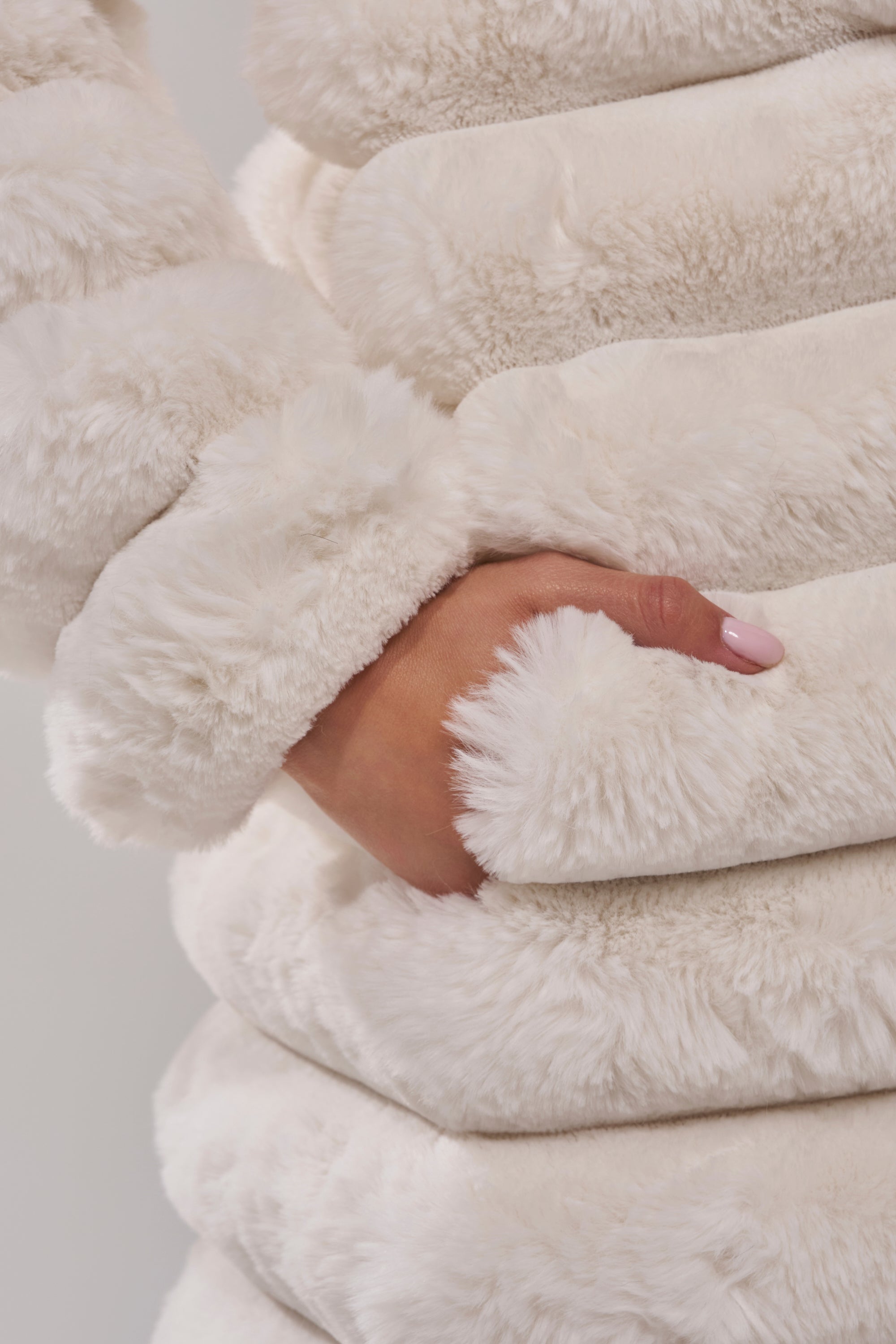 A close-up of a hand with light pink nails tucked into the pocket of the MAXI POPCORN FAUX FUR IN WHITE showcases its soft texture and stylish ribbed design.