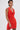 A person with short dark hair and hoop earrings wears the ALWAYS BEST DRESSED MINI DRESS IN RED—a sleeveless, curve-hugging halter dress. Visible tattoos on their shoulder and arm stand out against a plain light background.