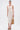 A woman stands against a plain background wearing the ALWAYS BEST DRESSED MIDI DRESS IN IVORY, styled with a woven tan handbag, brown platform sandals, and gold hoop earrings.