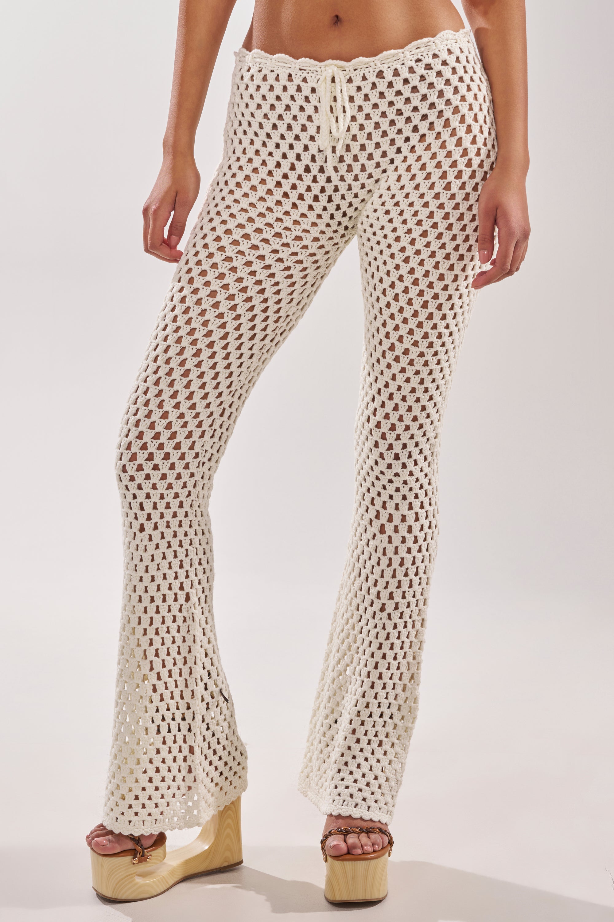Model shown from the waist down wearing BEACH VIBES CROCHET FLARED PANT in cream, featuring a drawstring waist and flared legs—styled with platform sandals for effortless resort-ready chic. 2
