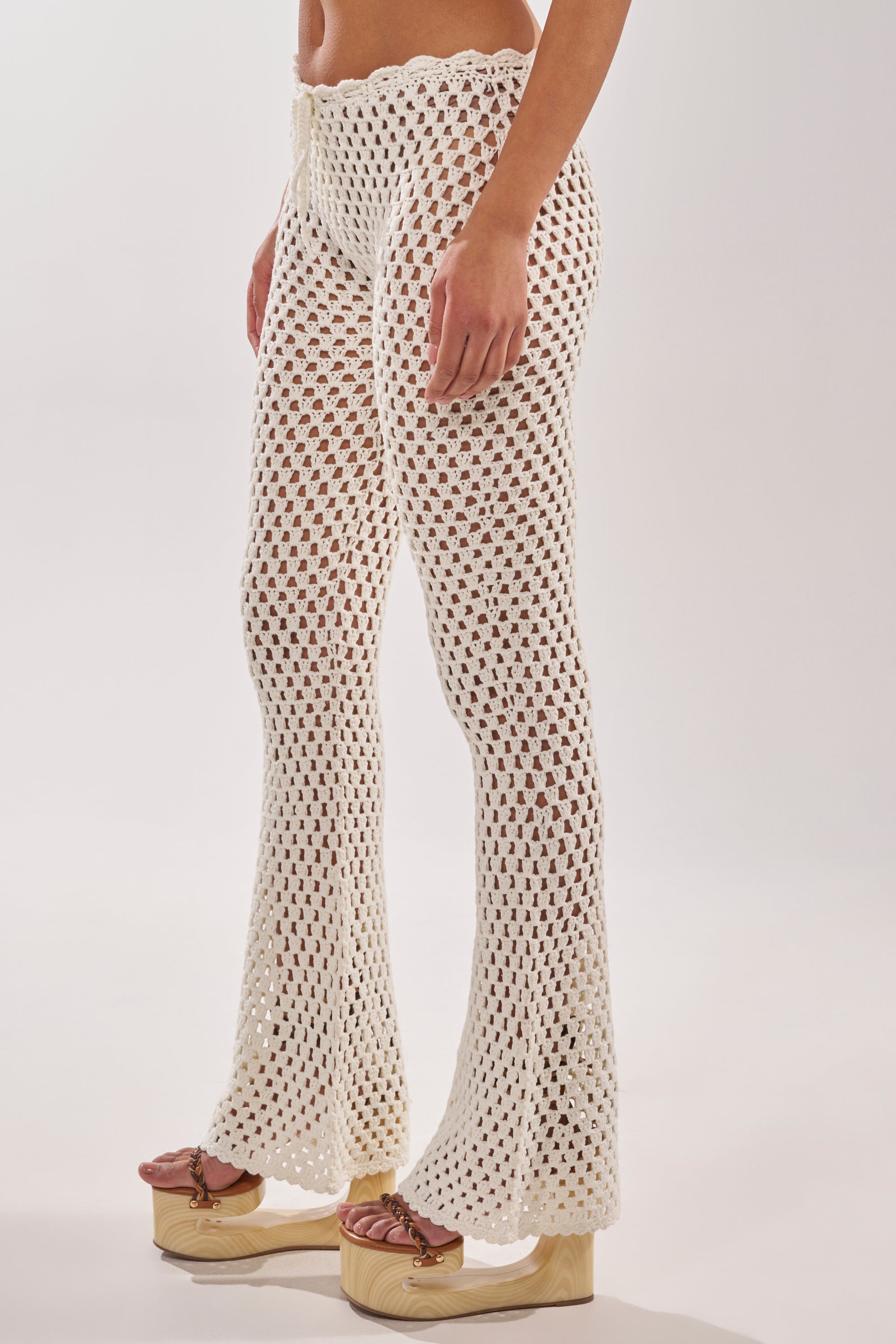 A person wears the BEACH VIBES CROCHET FLARED PANT with platform sandals. The plain, light background highlights these chic resort essentials. 3